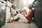 Champagne celebration, toast and senior couple having a drink to celebrate retirement on the floor of kitchen in home. Elderly man and woman happy on anniversary of marriage with cheers and alcohol