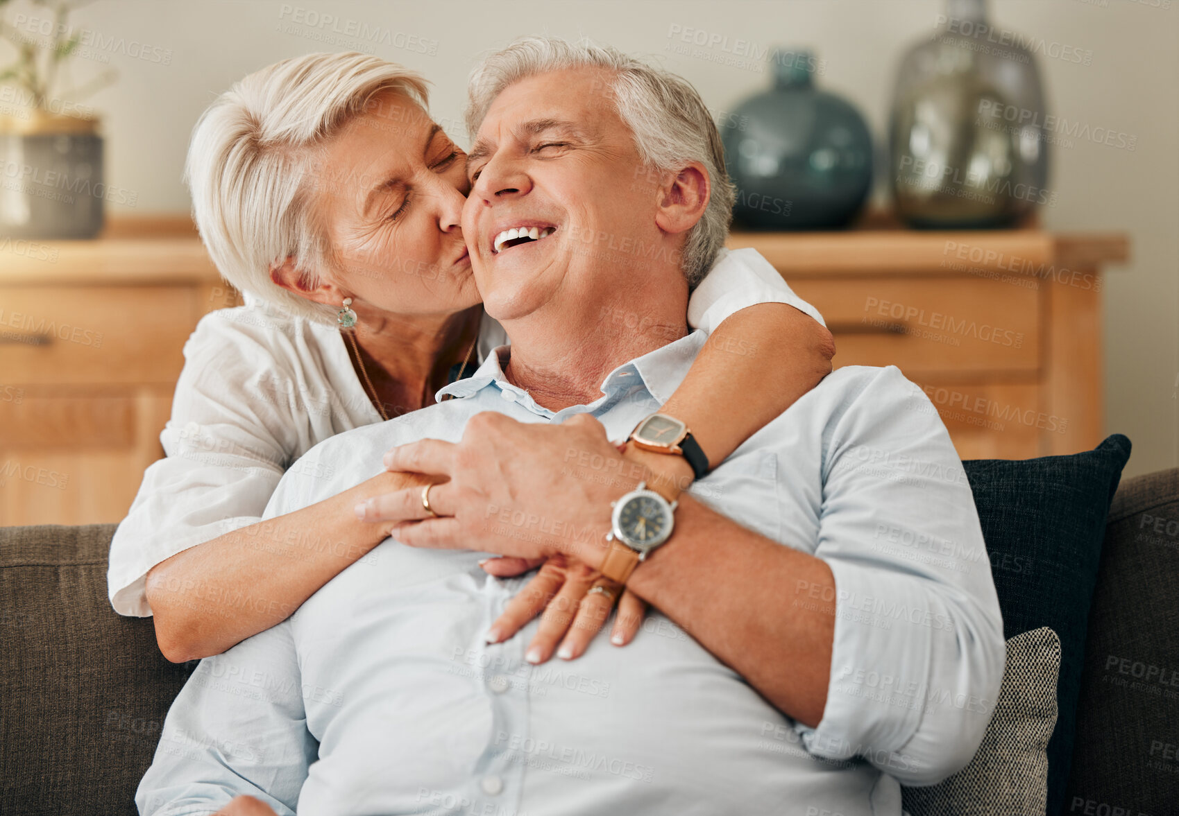 Buy stock photo Love, retirement and kiss with couple on sofa for support, trust and happy together. Relax, smile and lifestyle with old man and senior woman in living room together for embrace, marriage and hug 