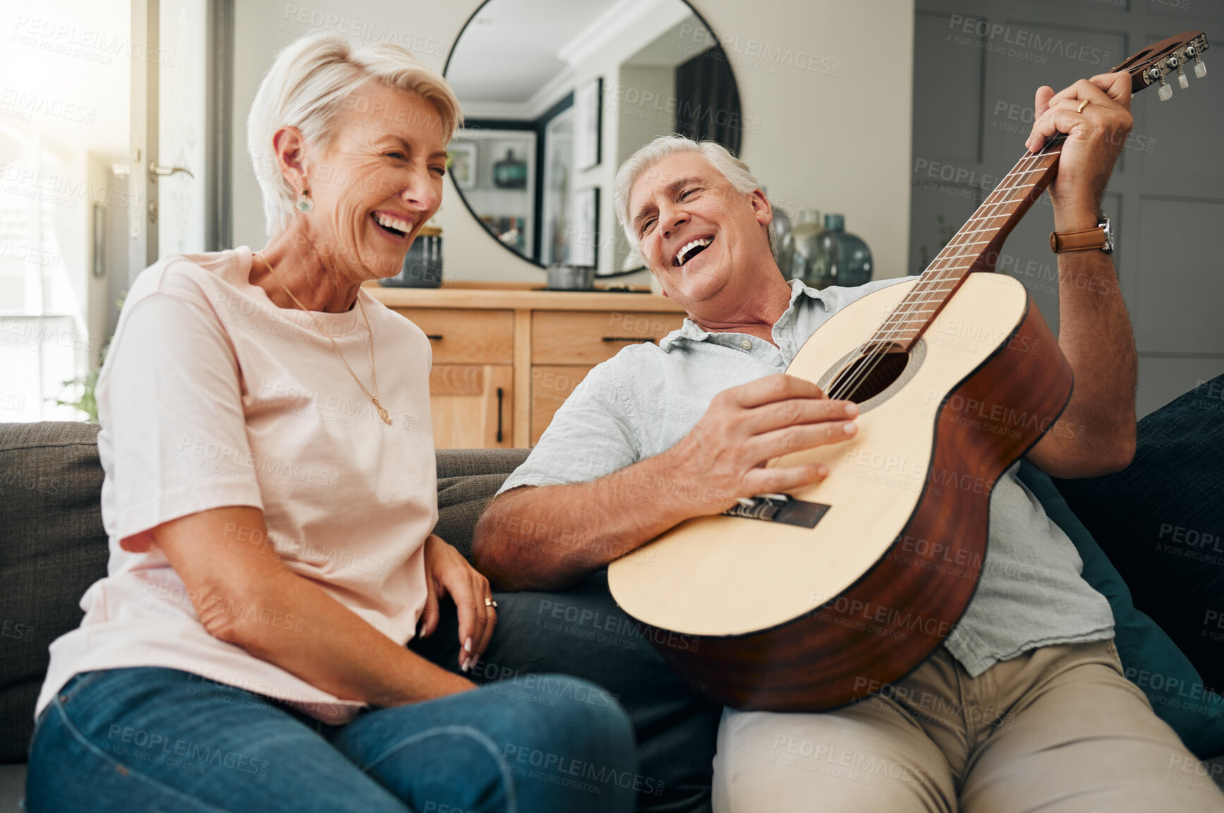 Buy stock photo Senior couple, guitar and romance while laughing and singing a romantic or funny song to wife sitting on the sofa at home. Happy old man and woman having fun during retirement in their texas house