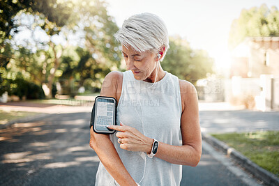 Buy stock photo Senior woman, fitness and phone armband listening to music for morning run in an urban street outdoors. Active elderly female runner checking smartphone to monitor training exercise or navigation