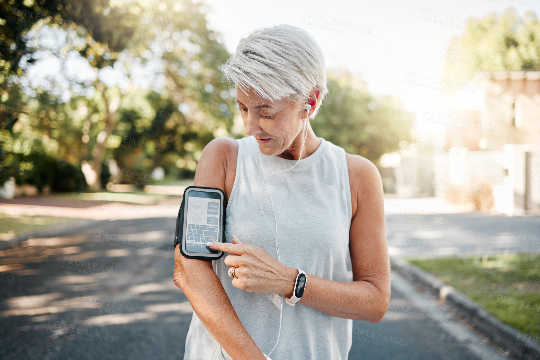 Buy stock photo Senior woman, fitness and phone armband listening to music for morning run in an urban street outdoors. Active elderly female runner checking smartphone to monitor training exercise or navigation