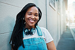 Black woman, smile and headphones on happy student girl on an urban or city street while smiling while leaning against a wall. Portrait of an African gen z female outside traveling in South Africa