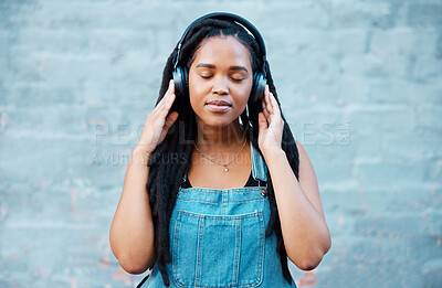 Buy stock photo Black woman, headphones and music with a girl feeling calm, relax and content listening to a podcast standing outside against city or urban wall. African female relaxed during mindful audio streaming