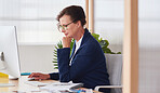 Mature business woman using computer in office working on creative graphic design project with photos of models on desk