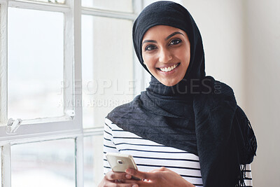 Buy stock photo Portrait muslim woman smiling using smartphone wearing hijab headscarf standing by window