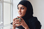 Beautiful muslim woman looking out window holding coffee wearing hijab headscarf