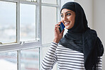 Muslim woman using smartphone talking on mobile phone looking out window wearing hijab headscarf