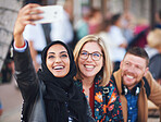Happy muslim woman taking photo with friends using smartphone camera in city