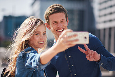Buy stock photo Happy young couple taking photo together using smartphone in city