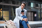Young business woman using smartphone listening to music wearing headphones texting with mobile phone sitting on steps in city