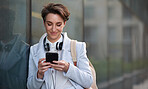 Young business woman using smartphone in city texting on mobile phone leaning on wall