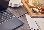 Restaurant, cafe or coffee shop table as a workspace with a laptop, papers and food in the morning. Background or closeup of a remote and wooden work desk outdoors at a fast food place