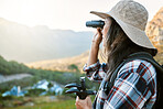 Hiking, exploration and mountain adventure with binoculars, trekking pole and walking aid in a remote landscape with view. Mature woman, hiker and tourist watching birdlife or wildlife in eco nature