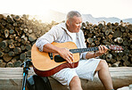 Mature man, relaxing and playing the guitar while sitting outdoors and enjoying his hobby while getting fresh air. Older man singing a song in his free time in retirement with a musical instrument