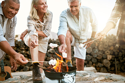 Camping, hiking and adventure senior people melting marshmallows in a camp fire during a nature retreat or getaway outdoors. Happy retired or senior group of friends enjoying fun recreation activity