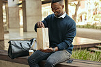 Office employee with a coffee, a paper sandwich bag and a smile, on a bench for a break from his busy work schedule. Happy, hungry businessman, time to eat, with his food and drink outside for lunch.