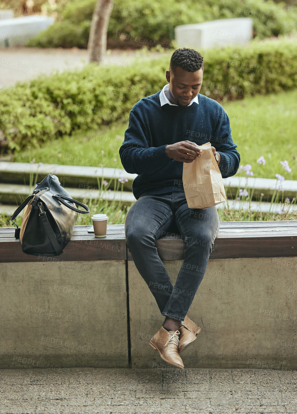 Buy stock photo Business man eating food for lunch on his break outdoors at a park opening a brown paper bag. Hungry, happy black male time to eat and drink outside in the city. Enjoying a takeaway or takeout meal