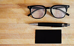 Above still life flat lay shot of glasses, spectacles, eyewear, a pen and a notepad, notebook on a wooden table, desk in a bright, modern corporate office in a business concept, setting