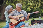 Music, guitar and a senior couple on picnic in park laughing with food, drinks and romance in retirement. Nature, love and elderly man and happy woman on romantic date on the grass on summer weekend.