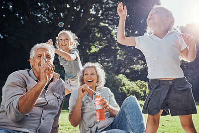 Buy stock photo Grandparents, kids and play with bubbles in the park, nature or outdoors. Love, smile and happy girls having fun, bonding and spending quality time with grandma and grandpa on grass with soap toy.
