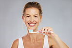Teeth, dental and oral hygiene with a woman brushing using a toothbrush and toothpaste in a studio on a gray background. Health, healthcare and face with a female taking care of her mouth and gums