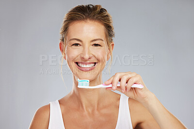 Buy stock photo Teeth, dental and oral hygiene with a woman brushing using a toothbrush and toothpaste in a studio on a gray background. Health, healthcare and face with a female taking care of her mouth and gums