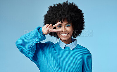 Buy stock photo Young, black woman and shows peace sign with blue studio background, trendy style and afro. Smile, happy and relax African American female, lady or girl influencer with casual fashion and cosmetics.