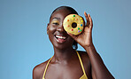 Beauty, black woman and portrait of donut on face with  blue studio wall for happy summer style. Matching, beautiful and fun african american girl with yellow makeup for quirky fashion campaign.