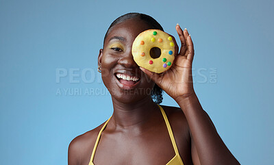 Buy stock photo Beauty, black woman and portrait of donut on face with  blue studio wall for happy summer style. Matching, beautiful and fun african american girl with yellow makeup for quirky fashion campaign.