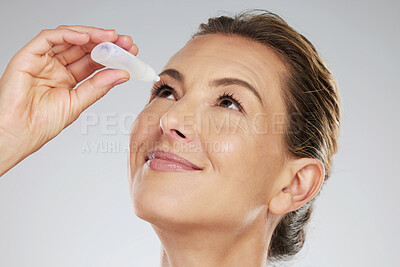 Buy stock photo Eye drops, eyes and care with a mature woman cleaning or washing her pupils in studio on a gray background. Health, hygiene and wellness with a female caring for her eye with a treatment product