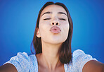 Woman face, blowing kiss and selfie portrait blue background for love emoji, relax and flirting on social media. Young girl beauty lips, mouth and funny expression of joy, happiness or summer style