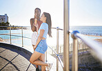 Girl friends have ice cream while out in the sun, on summer vacation at the pool and the ocean in the background. They are happy eating their dessert, while out in nature together. 