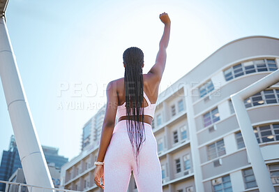 Buy stock photo Strong, empowerment and black woman for fitness, exercise and workout outside in city showing fist, motivation and power. African athlete female showing support against urban building in South Africa