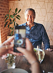 Senior man, phone and smile for picture on travel, vacation or restaurant experience while excited and happy at table. Elderly male tourist smiling for social media food post while traveling in Italy