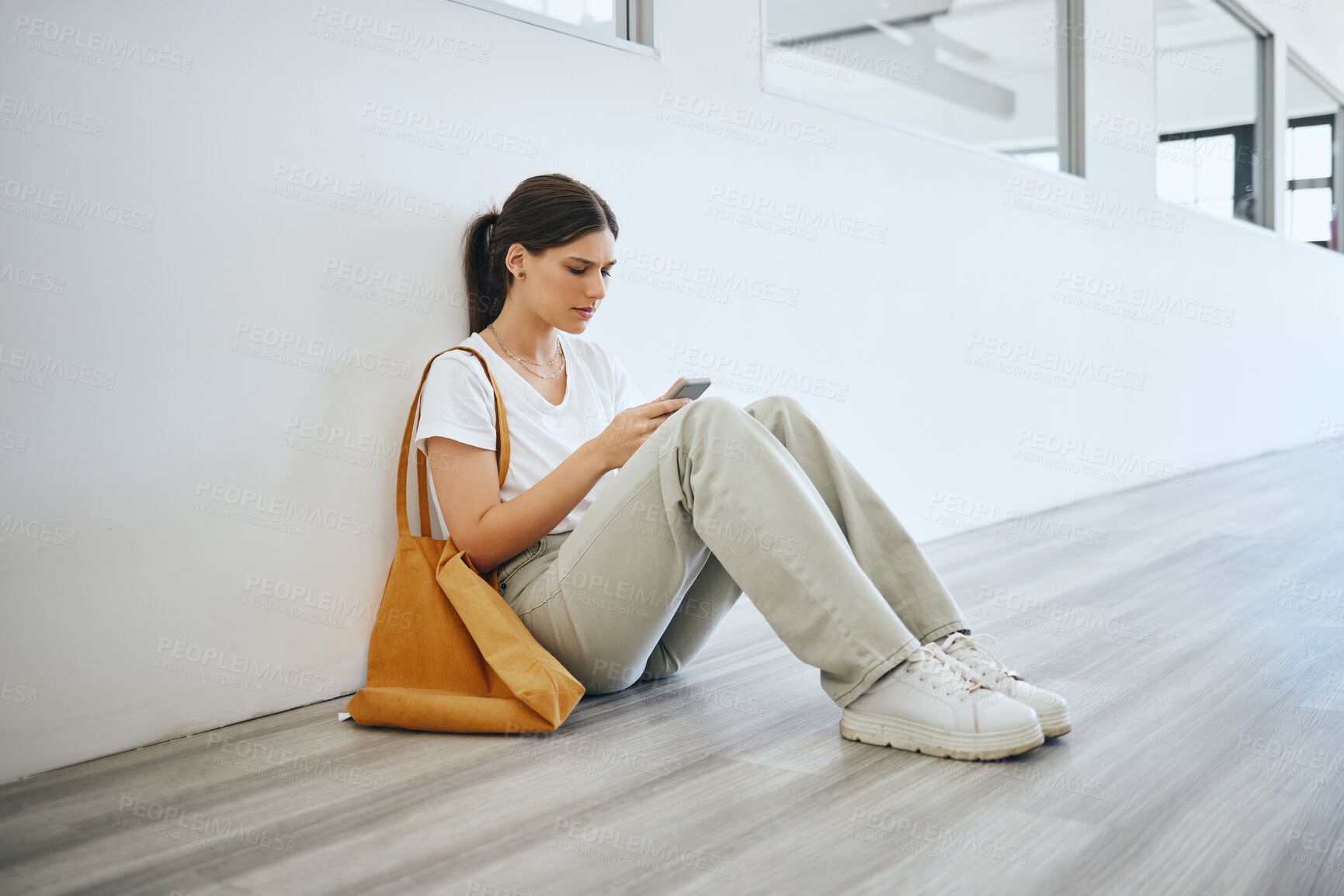 Buy stock photo Sad university woman, student alone on the floor in the hallway after class or lecture and browsing social media on smartphone. Academic depression, stress and anxiety from college education pressure