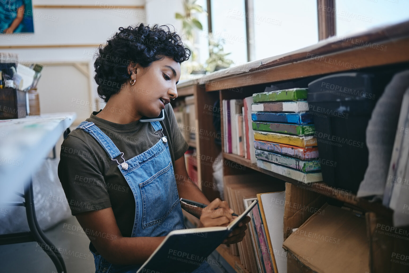 Buy stock photo Art, writing and woman on a phone call in her studio taking notes in a book. Businesswoman on smartphone, checking paint supplies and artwork in her workshop. Artist startup business for art class