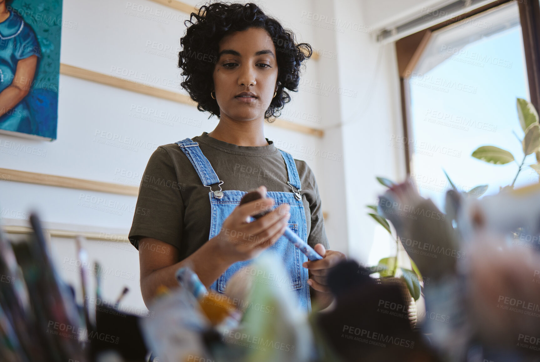 Buy stock photo Woman artist in her art workshop with paint brush and search for inspiration for artwork. Young, Indian professional painter, who is thinking in her studio about creativity and new ideas.