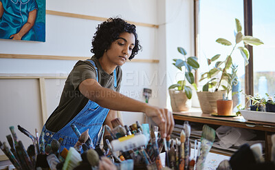 Buy stock photo Art, creative and painter with decision for brush while working on a painting in a studio for work. Indian woman, artist or designer picking a tool for oil paint job on a table in a workshop
