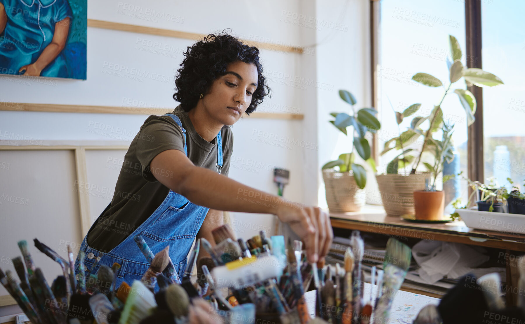 Buy stock photo Art, creative and painter with decision for brush while working on a painting in a studio for work. Indian woman, artist or designer picking a tool for oil paint job on a table in a workshop