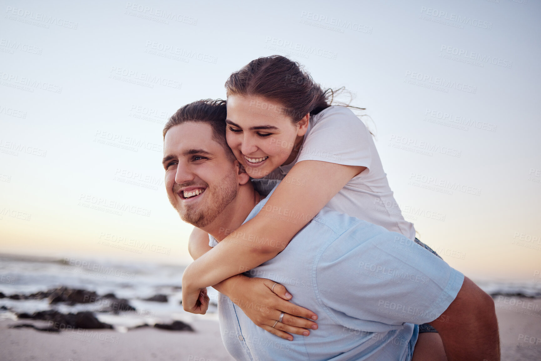 Buy stock photo Beach, love and couple with man carrying girl on his back, happy and smiling. Holiday, dating and romantic vacation by the sea. Young, real happy couple enjoying sunset, ocean and summer fun together