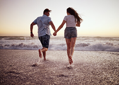 Buy stock photo Couple, beach and running, holding hands in waves at sunset on romantic holiday. Love, freedom and a man and woman on ocean vacation together. Sea, sunset and romance, happy guy and girl run in water