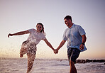 Beach water splash, couple and happy people together feeling love and fun in summer at sunset. Girlfriend and boyfriend holding hands in the ocean waves and sea on a vacation with quality time