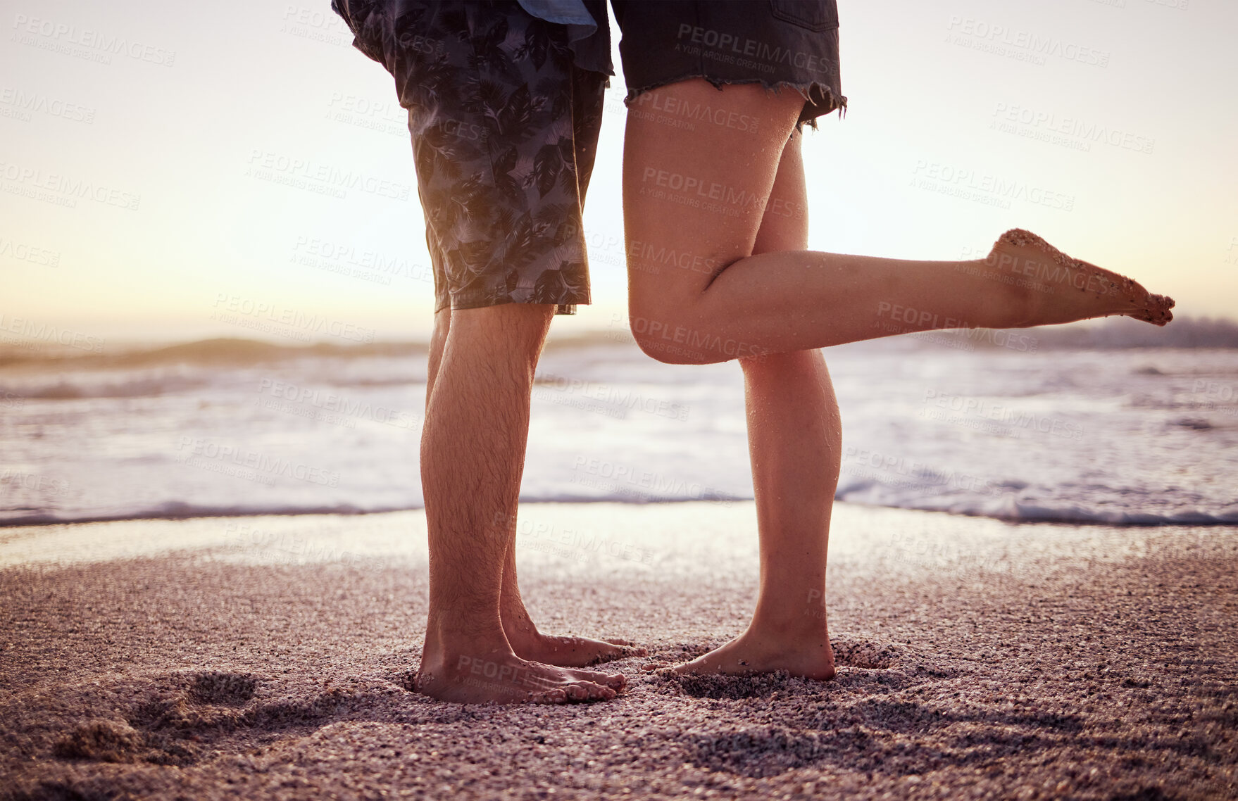 Buy stock photo Love, romance and legs on beach, couple in sunset on summer holiday together. Ocean, man and woman with feet in sand waiting for waves. Foot up, romantic hug and lovers at the sea in evening date.