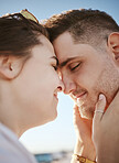 Love, touching face and couple on the beach, woman holding man with heads together. Summer, romance and loving happy couple by the ocean. Blue sky, holiday and people in love bonding by the sea