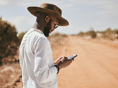 Buy stock photo Dessert dirt road, black man and phone text in nature on a vacation lost and waiting for a lift. 5g internet, mobile and web app usage of a person from Madrid wait for a taxi to travel in summer