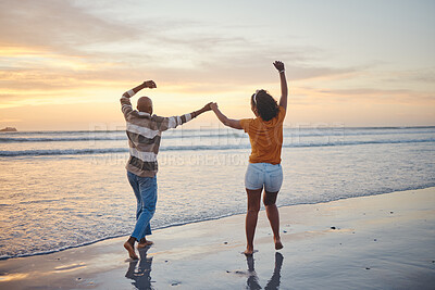 Buy stock photo Love, travel and happy couple at beach enjoying summer vacation or fun honeymoon at sunset while holding hands and being playful. Laughing, energy and seaside holiday with black man and woman at sea