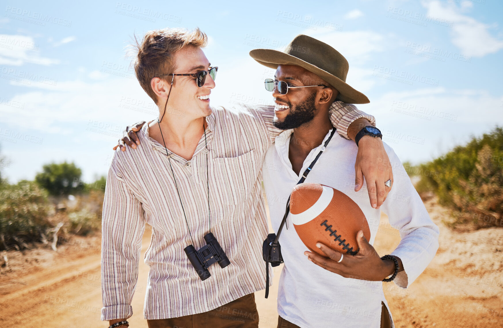 Buy stock photo Friends, binoculars and football in a desert with men on a safari tour, bonding and enjoying freedom in nature. Happy, diversity and explore with diverse people laughing, hug and travel together 