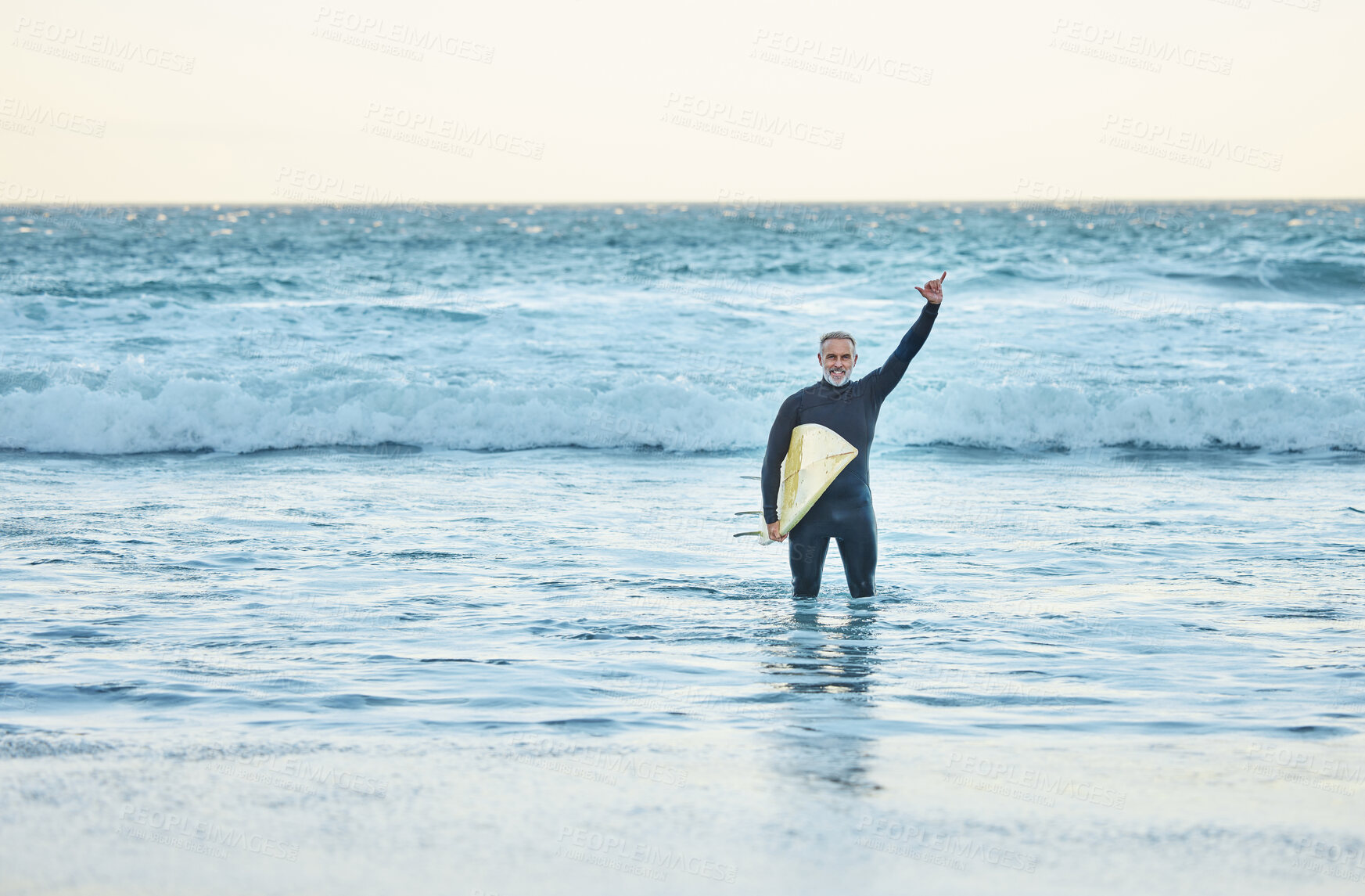 Buy stock photo Shaka, surf and sports with a mature man doing a hand gesture in the beach water during summer. Surfer, sea and nature with a male athlete in the ocean for workout, fitness or exercise in a wetsuit
