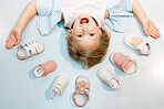 Child, shoes and happy by head on floor with smile on face against blue backdrop. Girl, sandal and mockup excited with happiness, color and summer fashion against studio background in Sweden