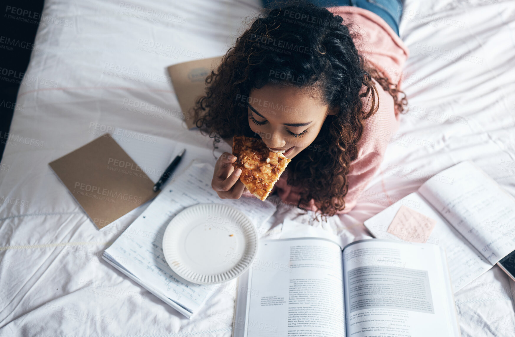 Buy stock photo Bed, girl and student studying with pizza for lunch in her bedroom reading school for tests or exams at home. Female enjoys fast food and learning from a notebook and university or college textbooks